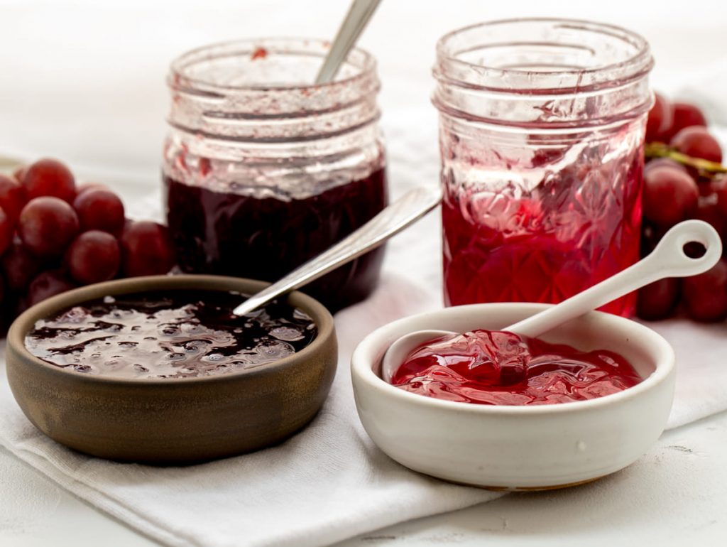 one brown bowl filled with grape jam and a white bowl filled with grape jelly