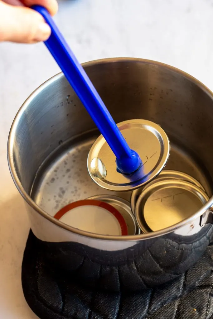 Mason jar lids in a saucepan with hand reaching in with canning magnetic wand