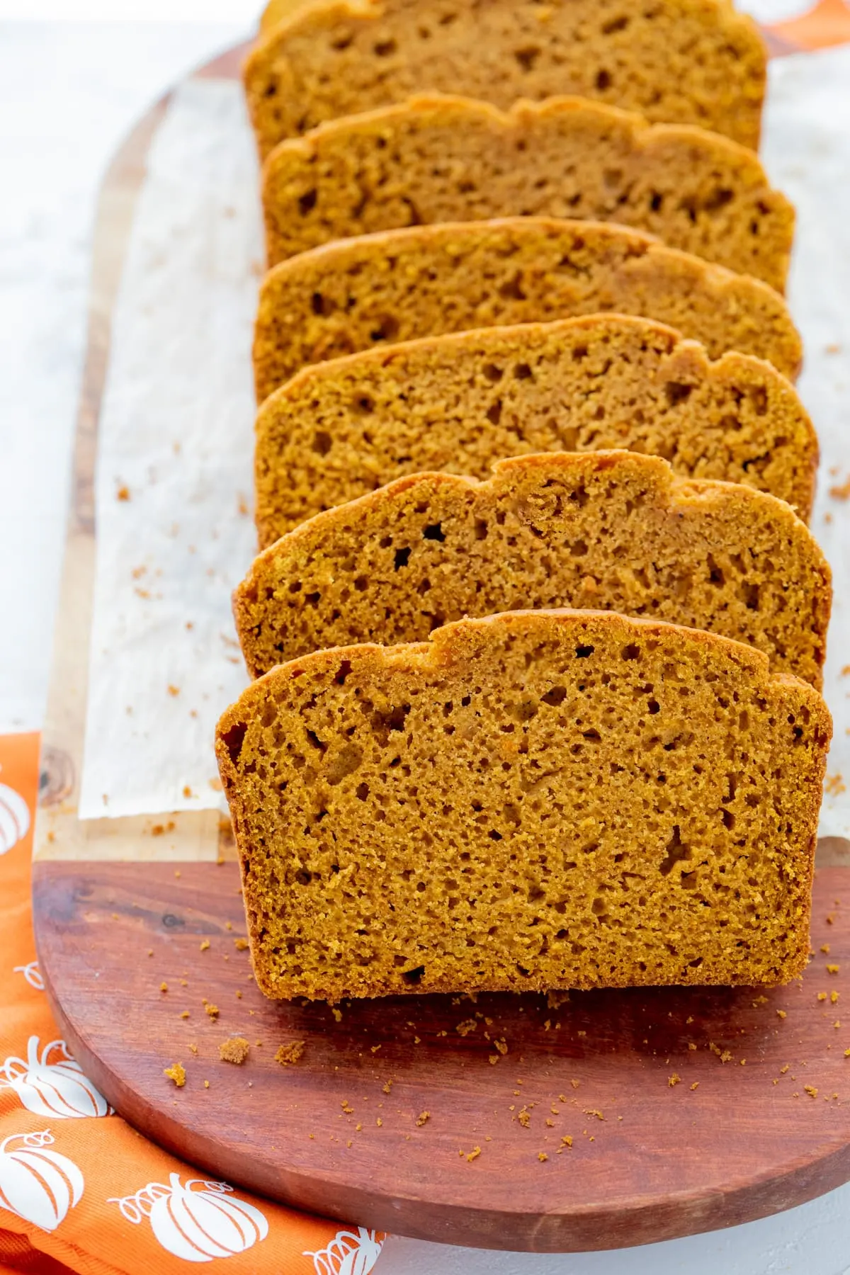 Slices of pumpkin bread on white parchment and wooden cutting board