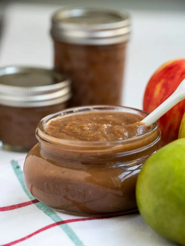 Apple pear butter in a small mason jar on a white towel next to pears and apples