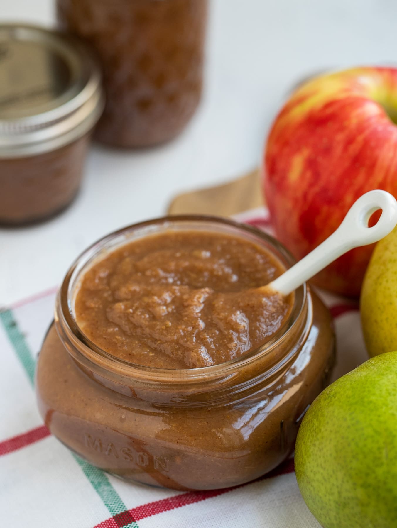 Apple pear butter in mason jar with white spoon next to pears and apples