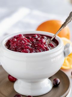 white bowl of cranberry sauce with oranges and silver spoon