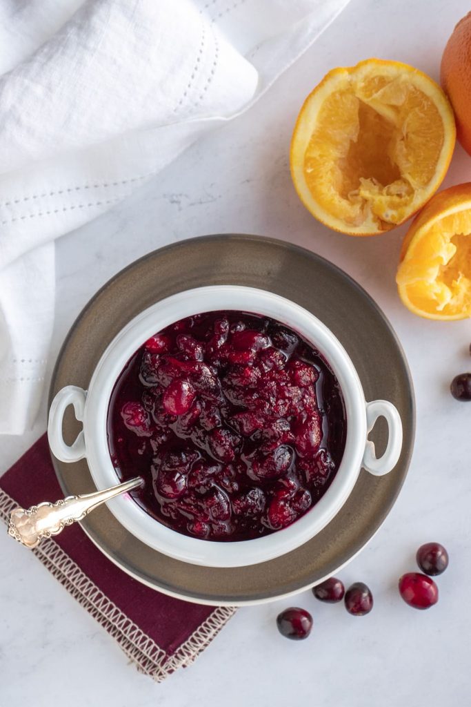 overhead view of bowl of cranberry sauce with fresh berries and squeezed oranges