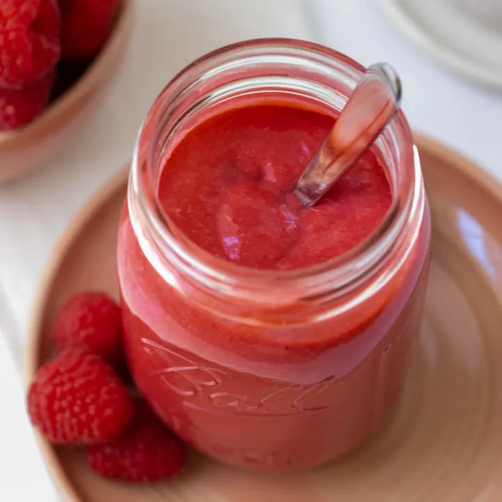 open mason jar with raspberry curd and silver spoon