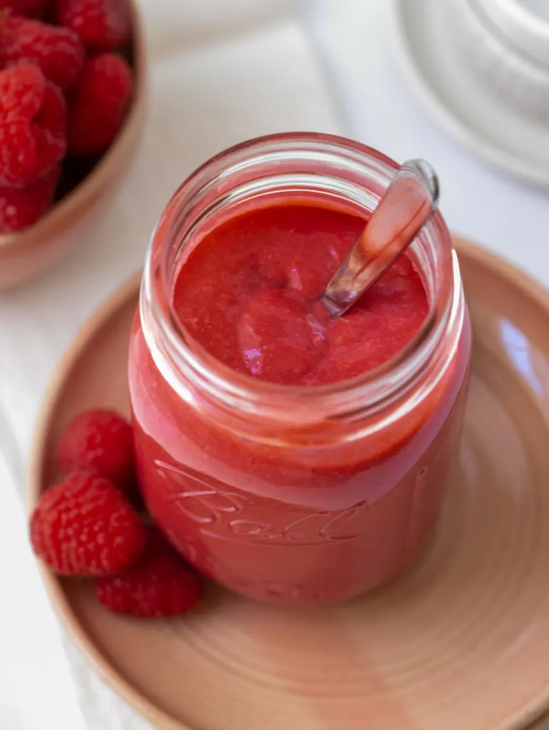 overhead view of filled mason jar with raspberry curd on pink plate and fresh berries