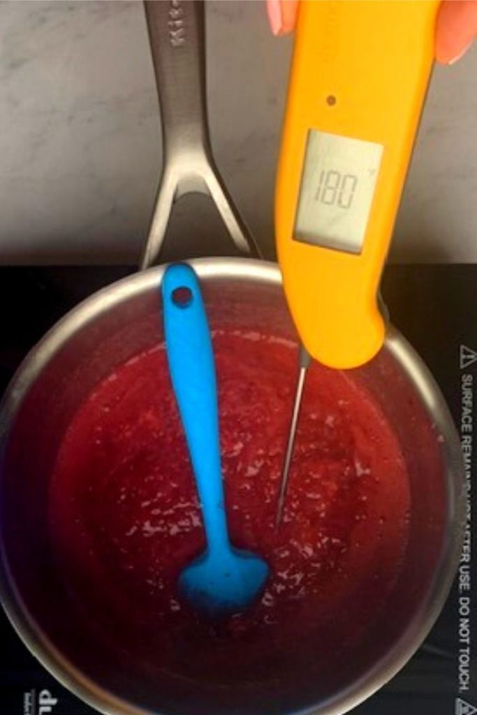 food thermometer in the raspberry curd mixture as it cooks in a saucepan