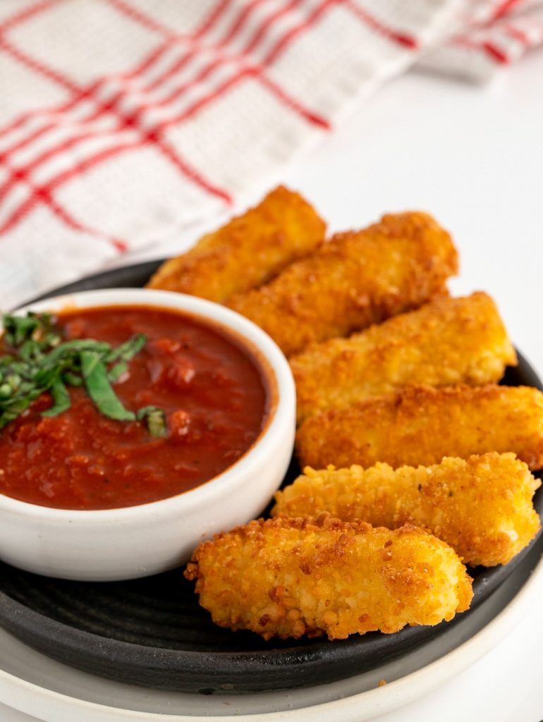 Pan fried mozzarella sticks on black plate with marinara sauce in a bowl