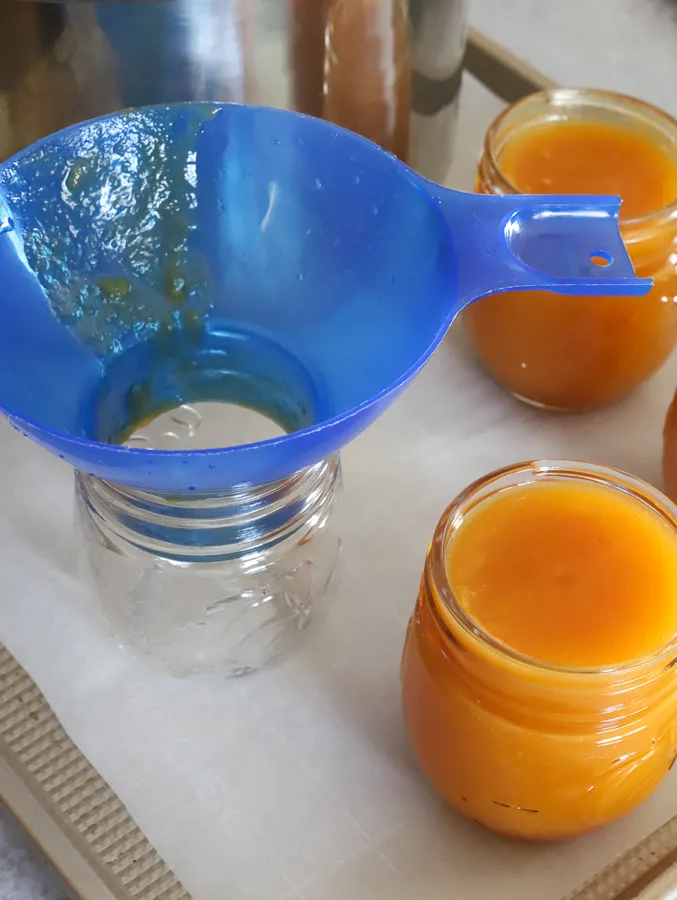 Fresh peach butter ladled into mason jar with canning tools and funnel