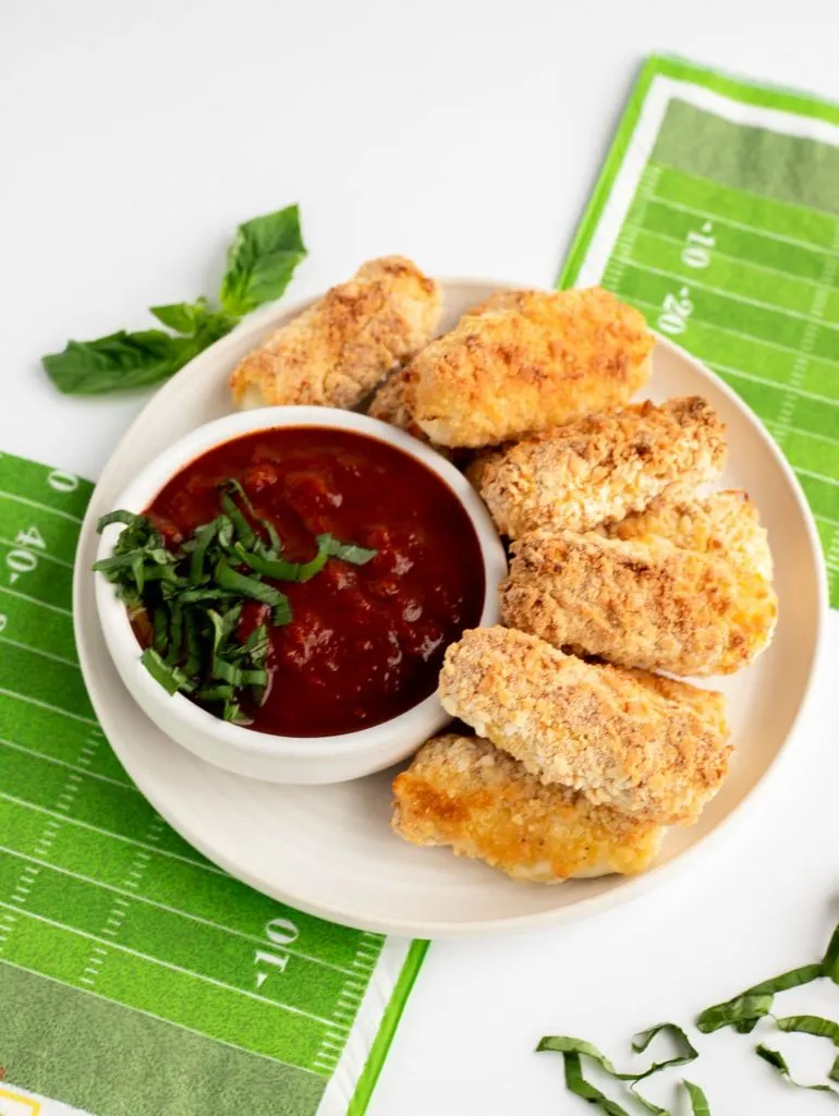 Baked mozzarella sticks on white plate with marinara sauce and green football field napkin