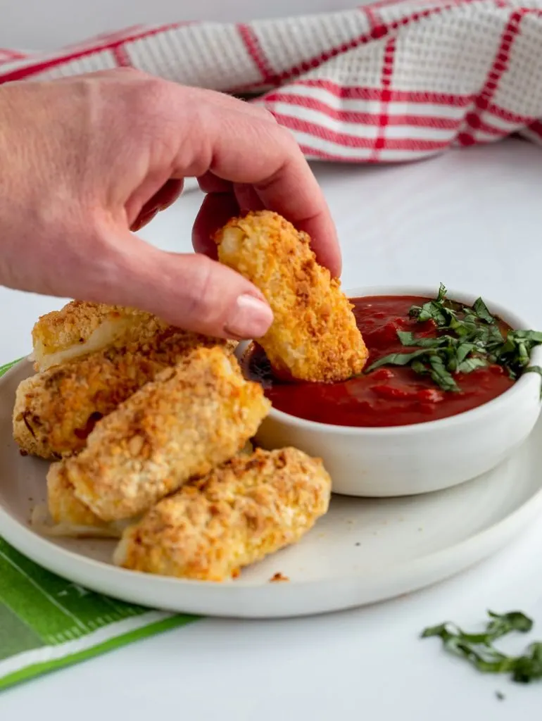 baked mozzarella sticks being dipped into a marinara pasta sauce with basil