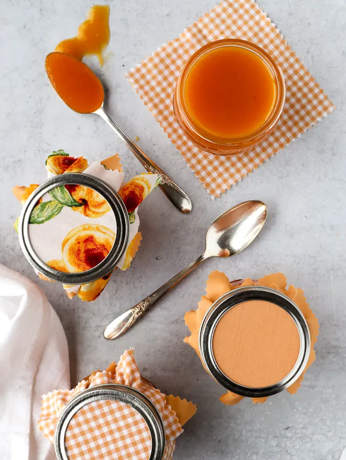 overhead view of peach butter with four mason jars filled and a spoonful of peach butter on the surface