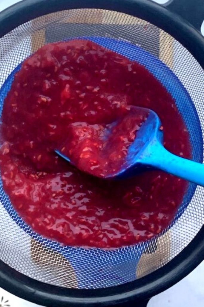 raspberry curd with seeds on a sieve on top of a canning funnel and mason jar