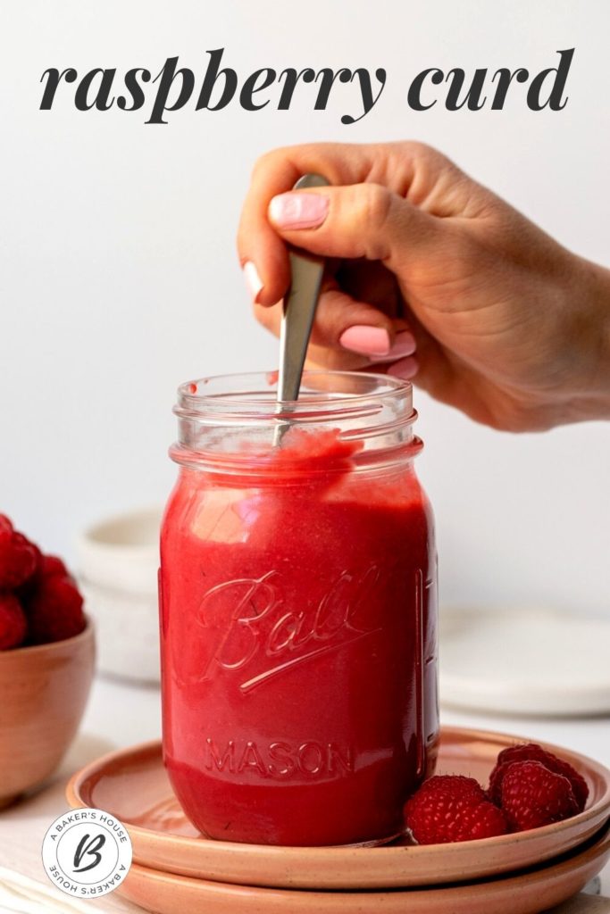 hand reaching into jar of raspberry curd with spoon