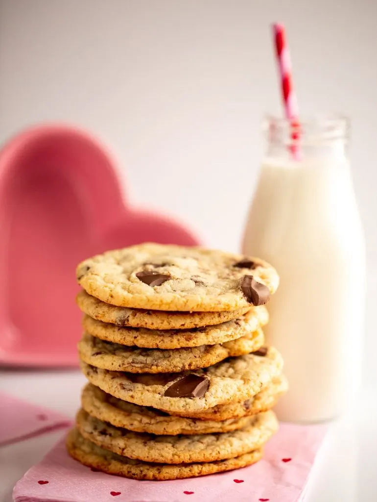 stack of chocolate chip cookies next to glass of milk