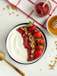 overhead view of creamy yogurt with jam, granola and berries in black bowl