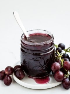 jar of grape jam with fresh grapes on white plate