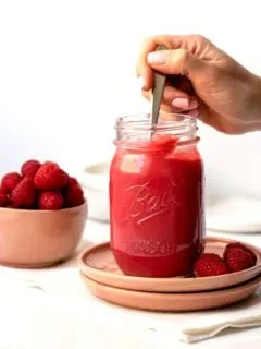 hand holding spoon that is dipped into a jar full of bright pink raspberry curd