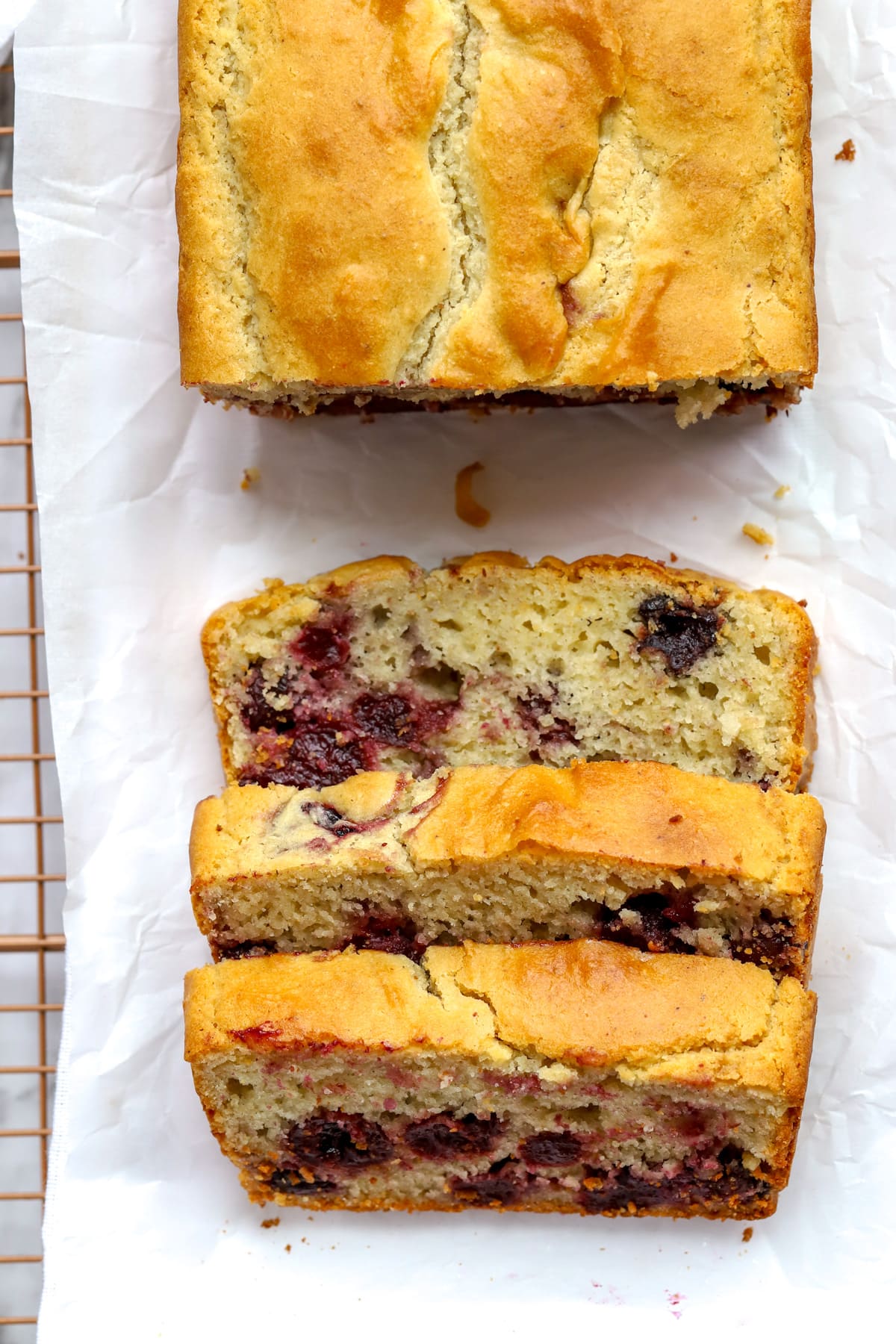 Overhead view of baked cherry bread on parchment paper with slices of bread with cherries