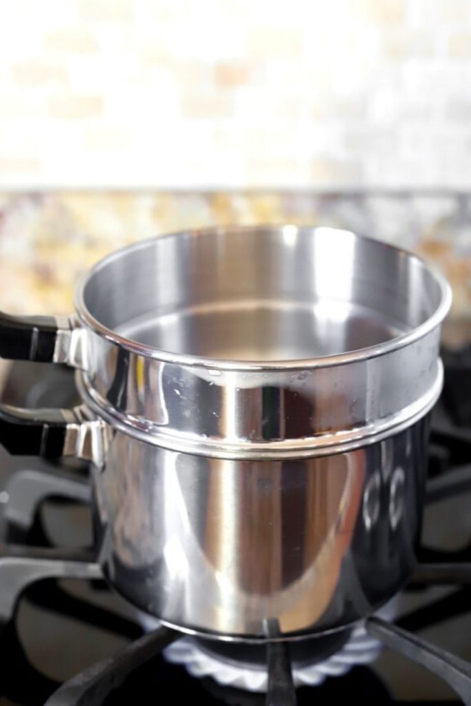 A double boiler sits on the stovetop with the gas lit