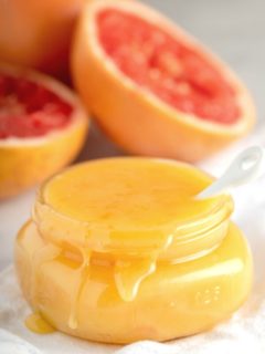 overflowing jar of grapefruit curd with fresh grapefruits in background