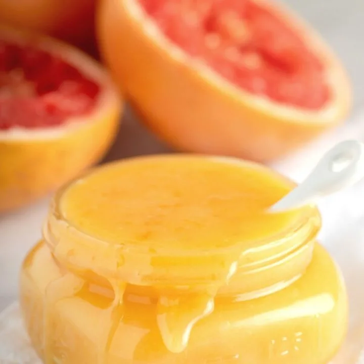 overflowing jar of grapefruit curd with fresh grapefruits in background