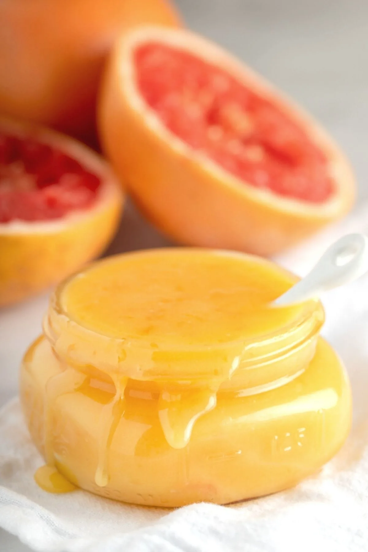 overflowing jar of grapefruit curd with fresh grapefruits in background