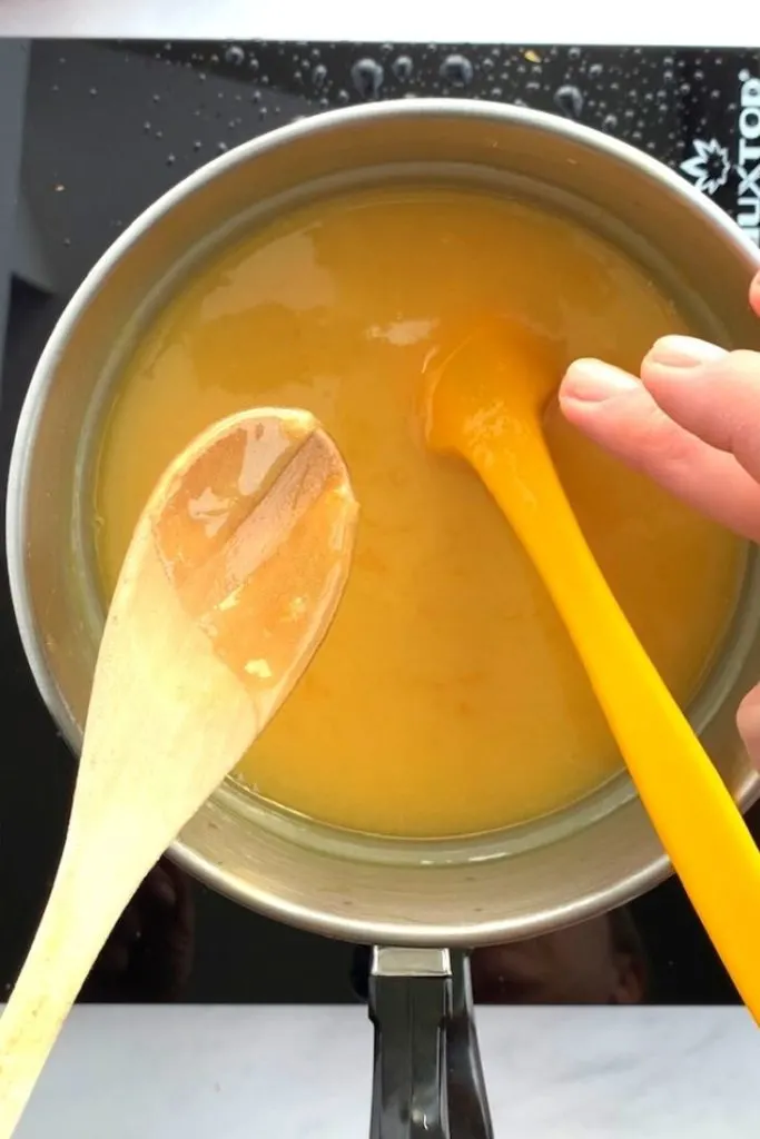wooden spoon and yellow spatula used to stir yellow grapefruit curd in saucepan
