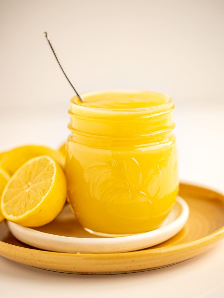 bright yellow jar of lemon curd on white and yellow plates with fresh lemons