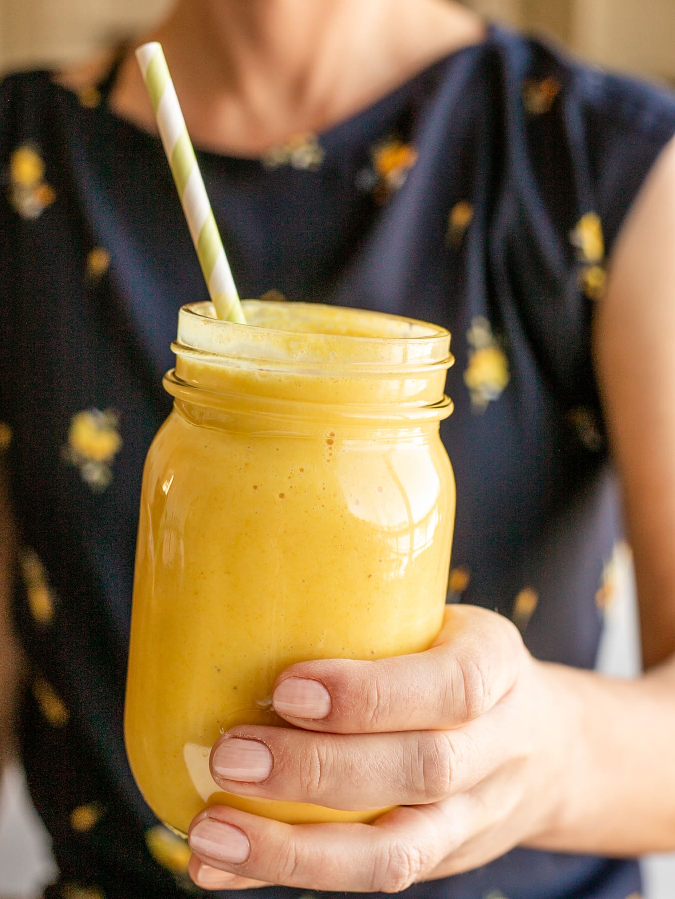 person in blue flowered shirt holding ou mason jar cup of yellow smoothie