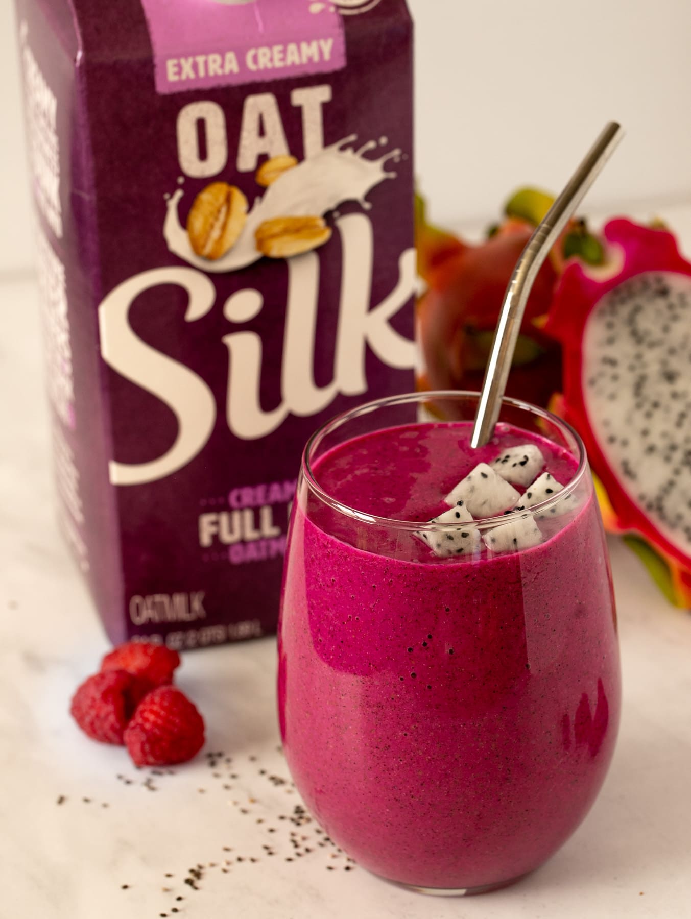 Dragon fruit smoothie in a glass with silver straw and Silk Oatmilk