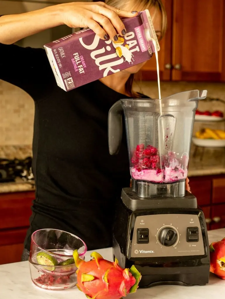 person pouring Silk Oatmilk into blender with dragon fruit and other ingredients
