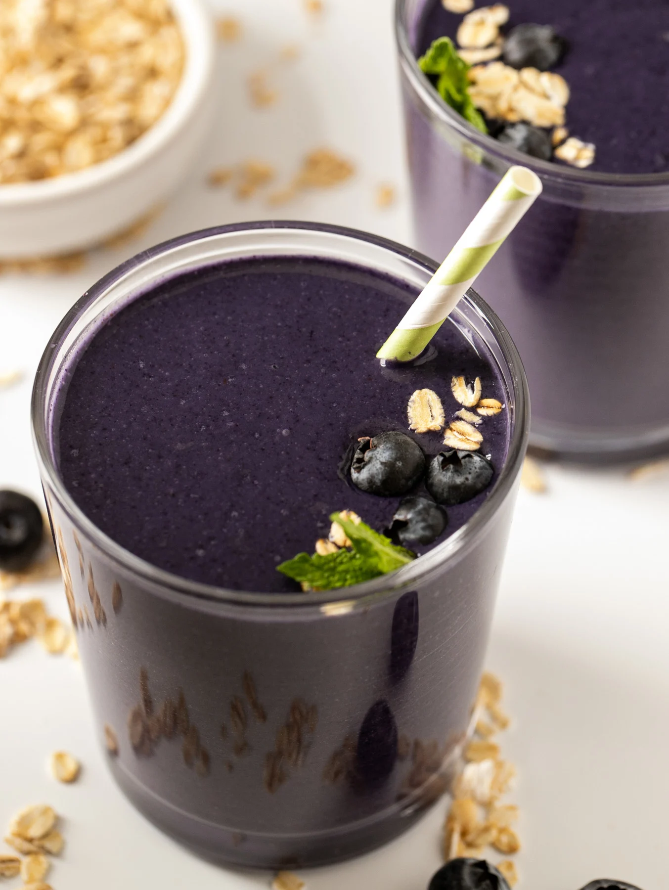 glass of dark blue blueberry oatmeal smoothie with oats and berries