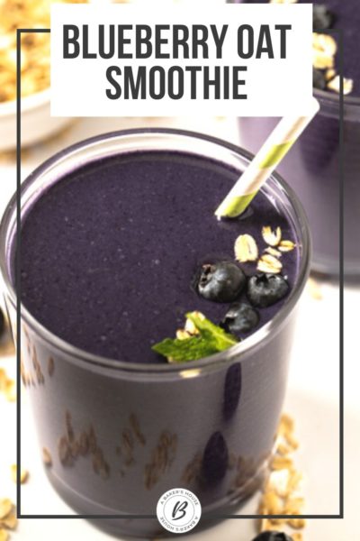 Glass filled with dark blue smoothie with blueberries, oats and oatmilk with green and white striped straw