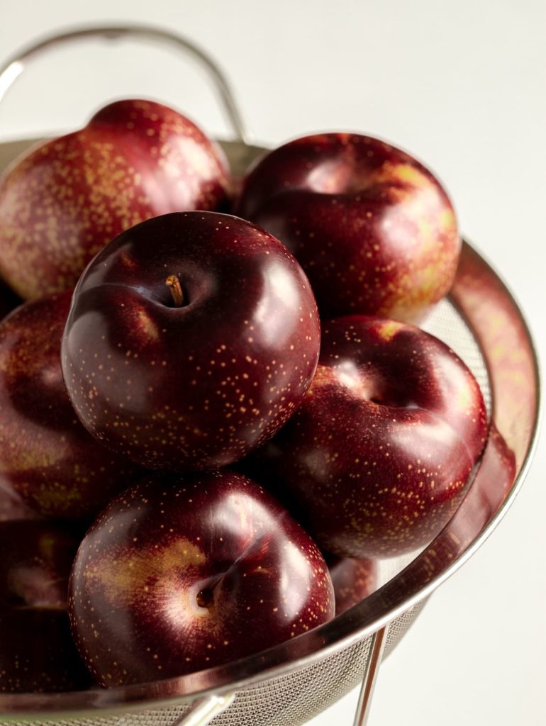 Fresh plums piled high in a metal strainer