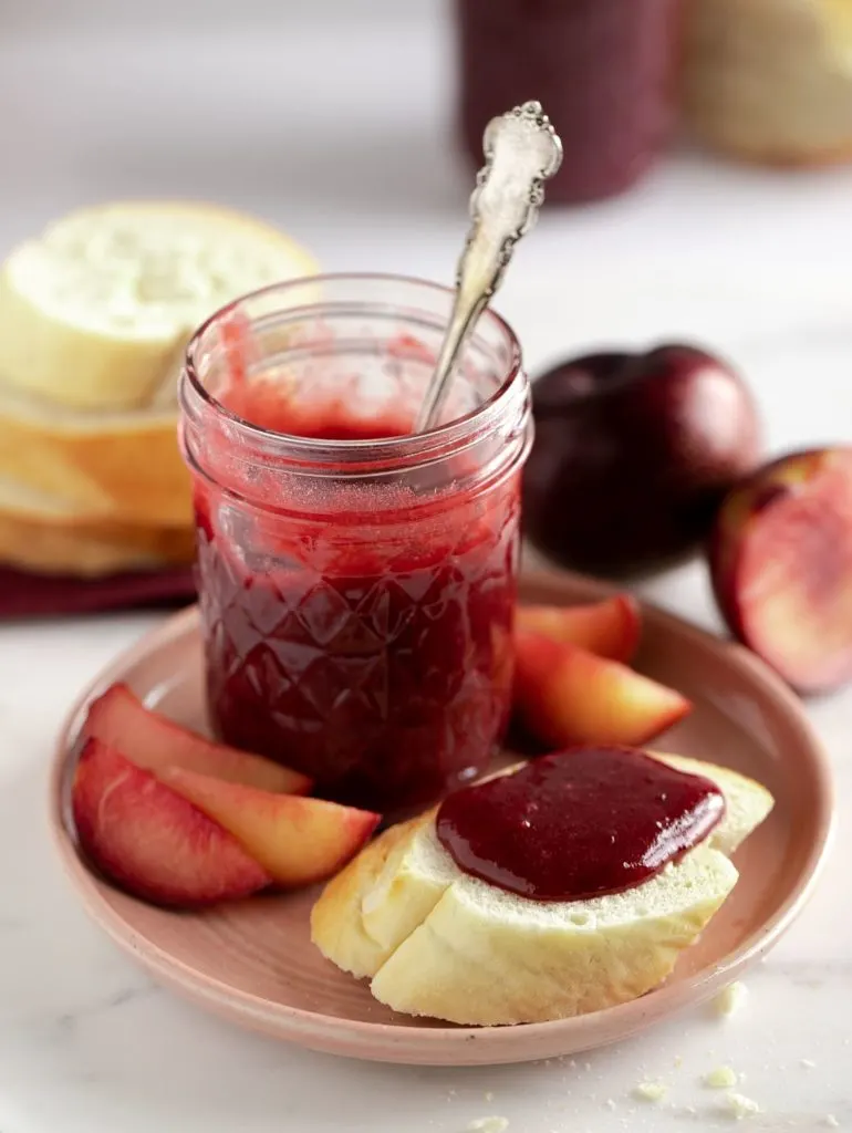 plum butter spread on slice of bread on pink plate next to jar of plum butter and fresh plums